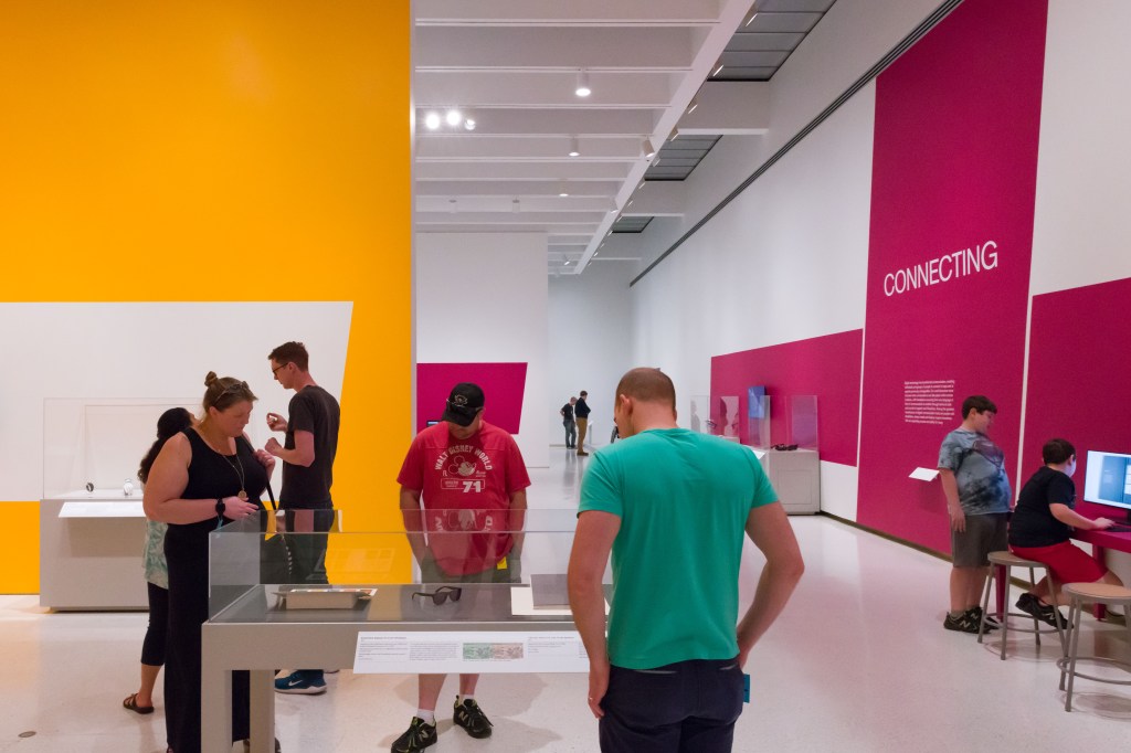 visitors gather around a display case containing glasses