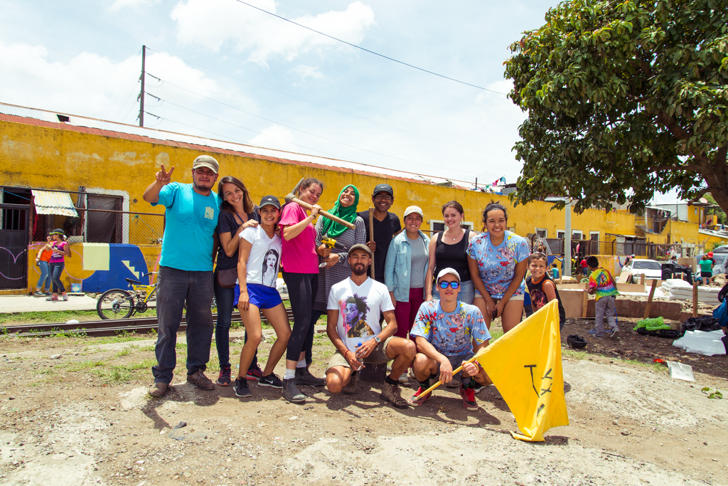 a group of people 11 posing on a sunny day, one person holding a yellow flag and another holding a mallet