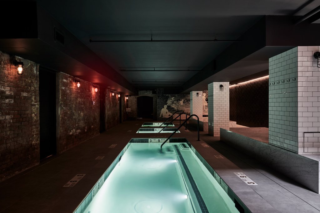 rows of pools in a dark room with a low dark ceiling, brick walls, and red lighting fixtures