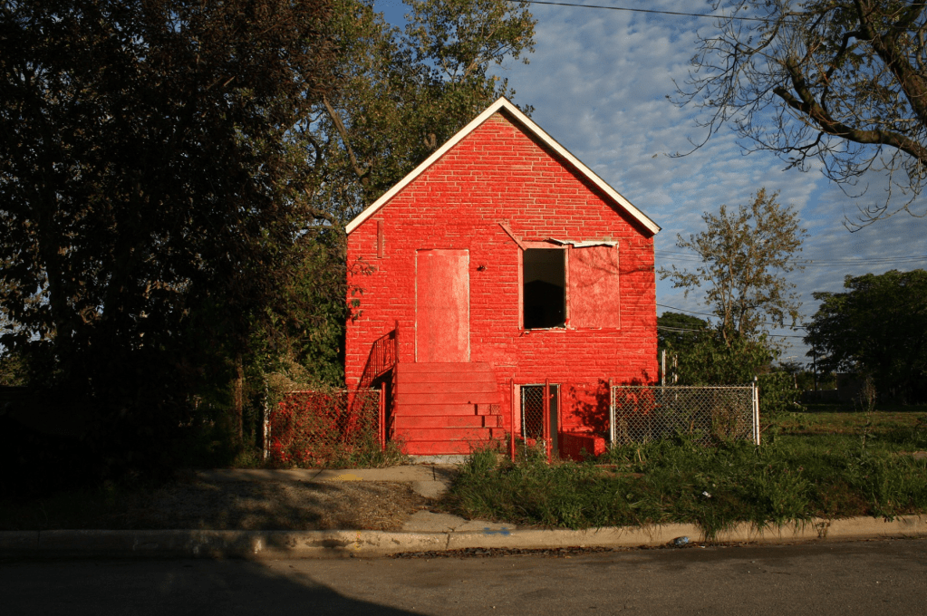 a building with a sealed door and window with no frame surrounded by trees on one side - the entire building (including steps) has been painted red - the color of Harold's Chicken Shack