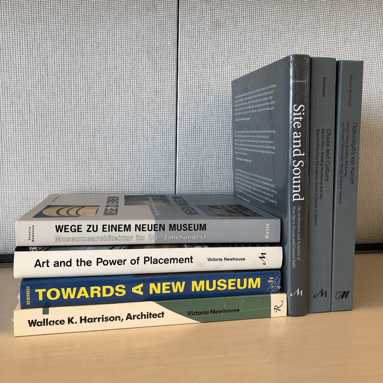 A stack of white, gray, and a blue books with the titles: Wallack K. Harrison Architect, Towards A New Museum, Art and the Power of Placement, Site and Sound, and Chaos and Culture. 2 books are in German.