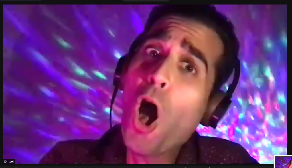 a dj wearing headphones is captured mid shout, with colorful disco lights bouncing off the wall behind him