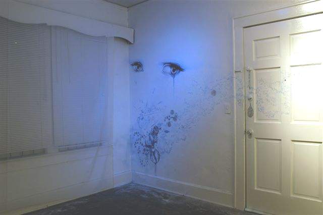 in the corner of a completely white room, there are two realistic eyes painted on the wall. the eyes are crying, and underneath is a trail of art that moves from the wall to the door