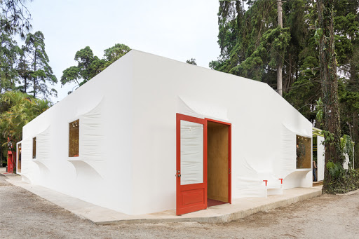 a white stucco rectangular house with protruding white square windows and a bright red door