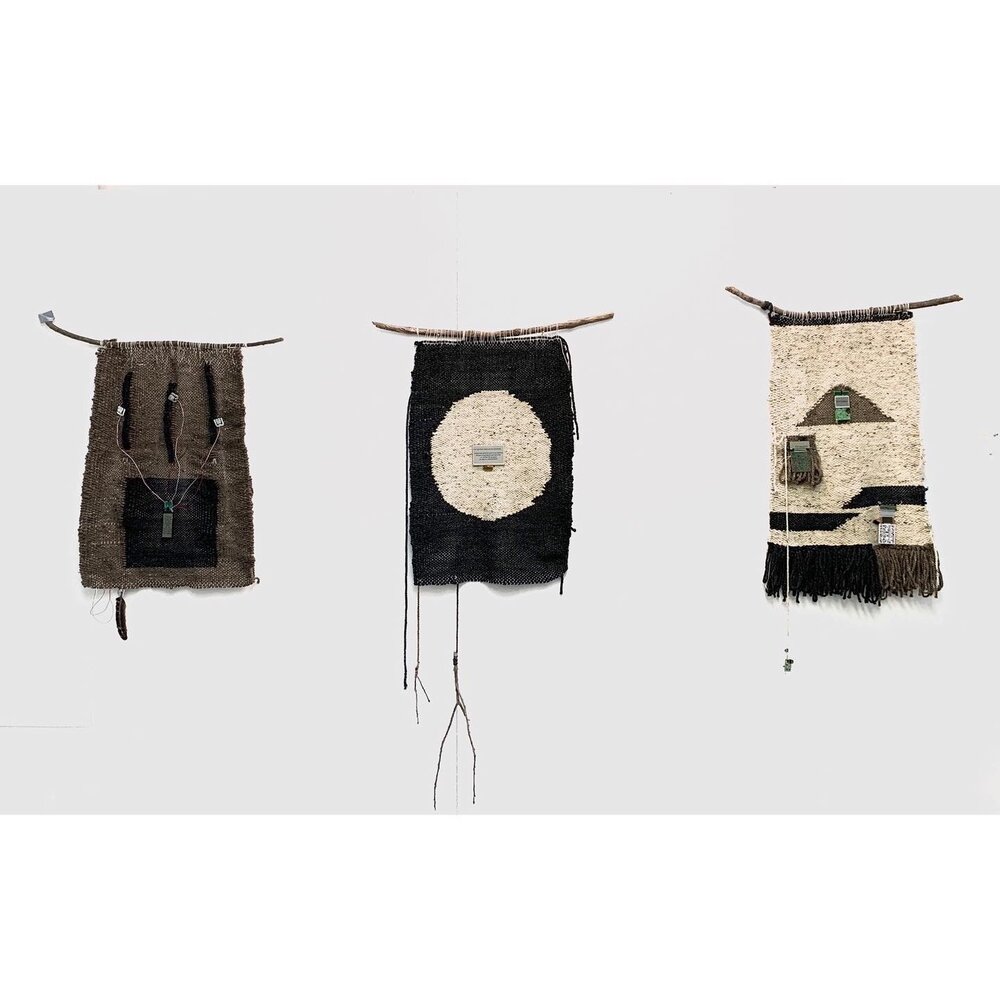  three small rectangular tapestries are woven with brown, black, and white earth toned fibers. They are displayed hanging from sticks. 